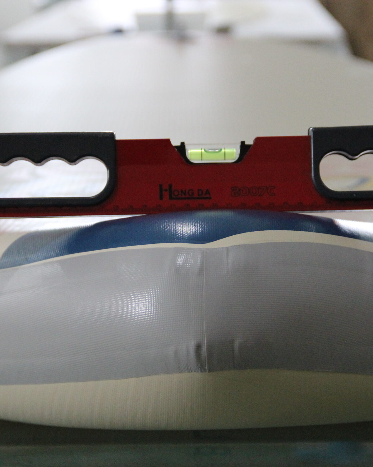 A spirit level laid across an inflated white paddle board during a shape check.